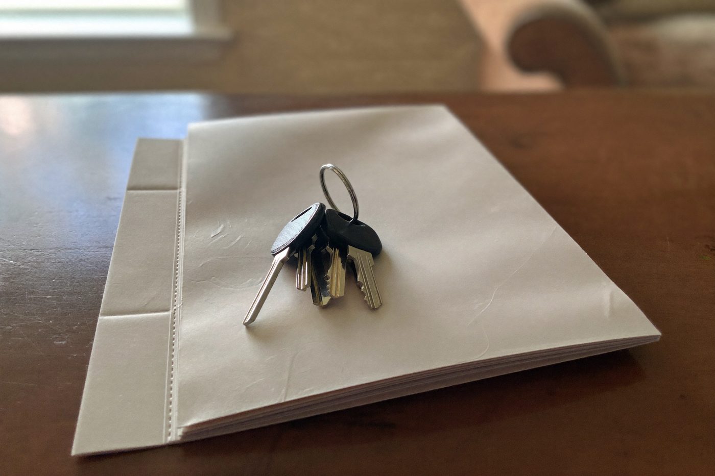Un trousseau de clés posé sur une pochette cartonnée fermée, sur une table en bois