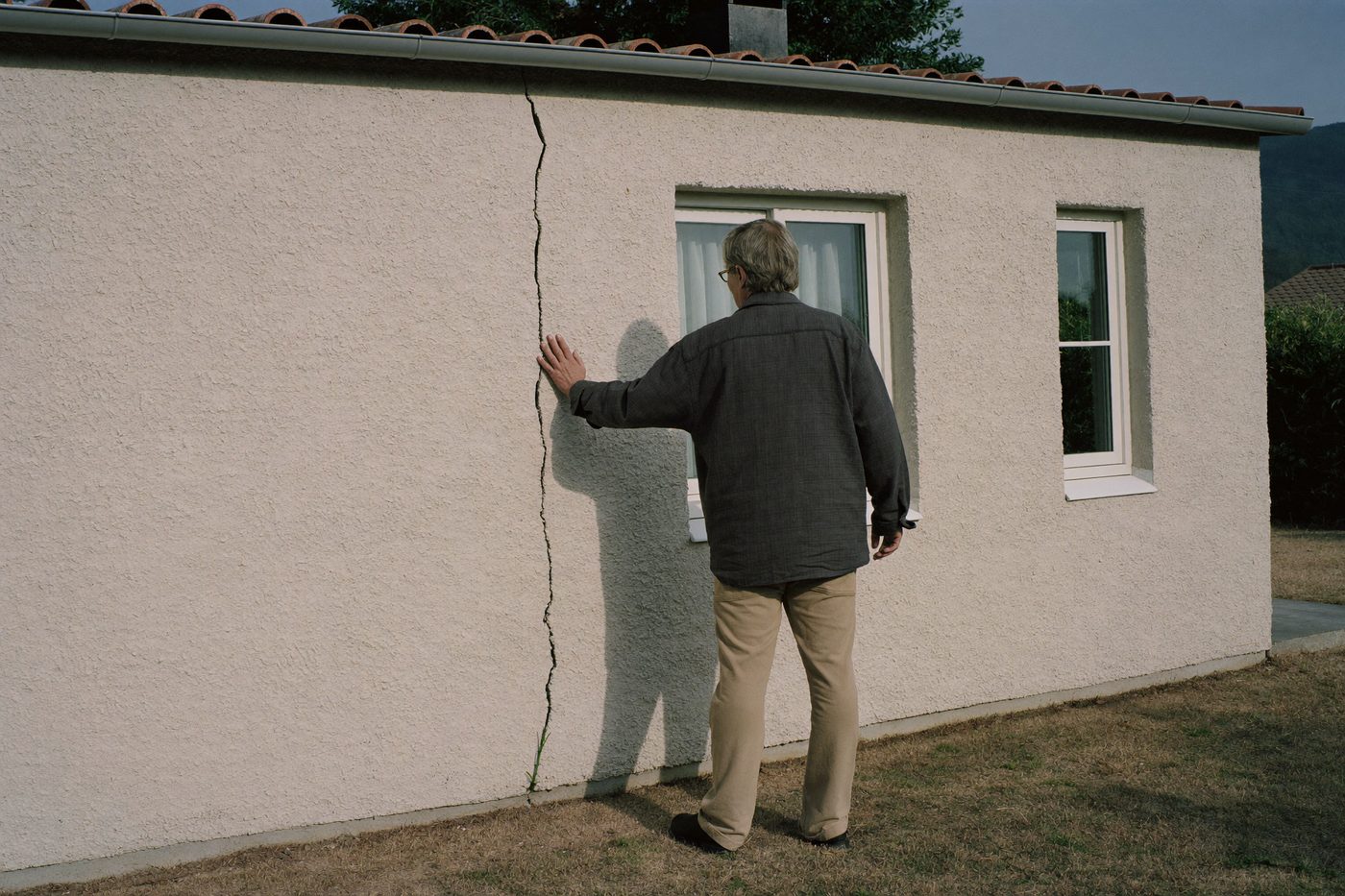 Propriétaire de dos, la main sur la fissure qui traverse la façade de son pavillon — illustration générée