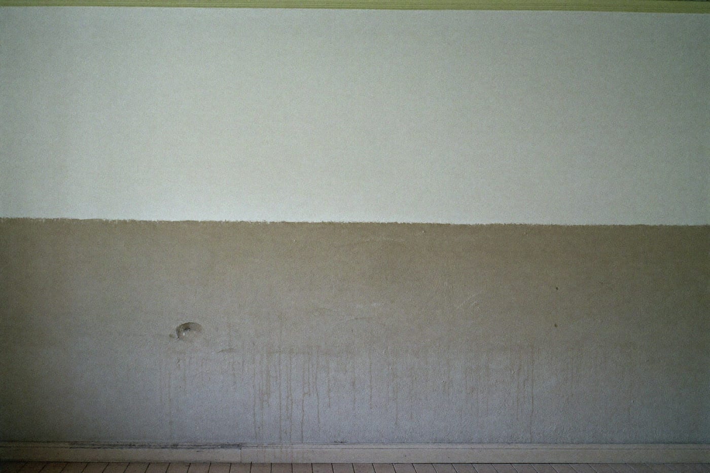Mur intérieur d’une pièce vide : la partie basse est ternie et grisée, la partie haute est restée claire, séparées par une limite horizontale nette