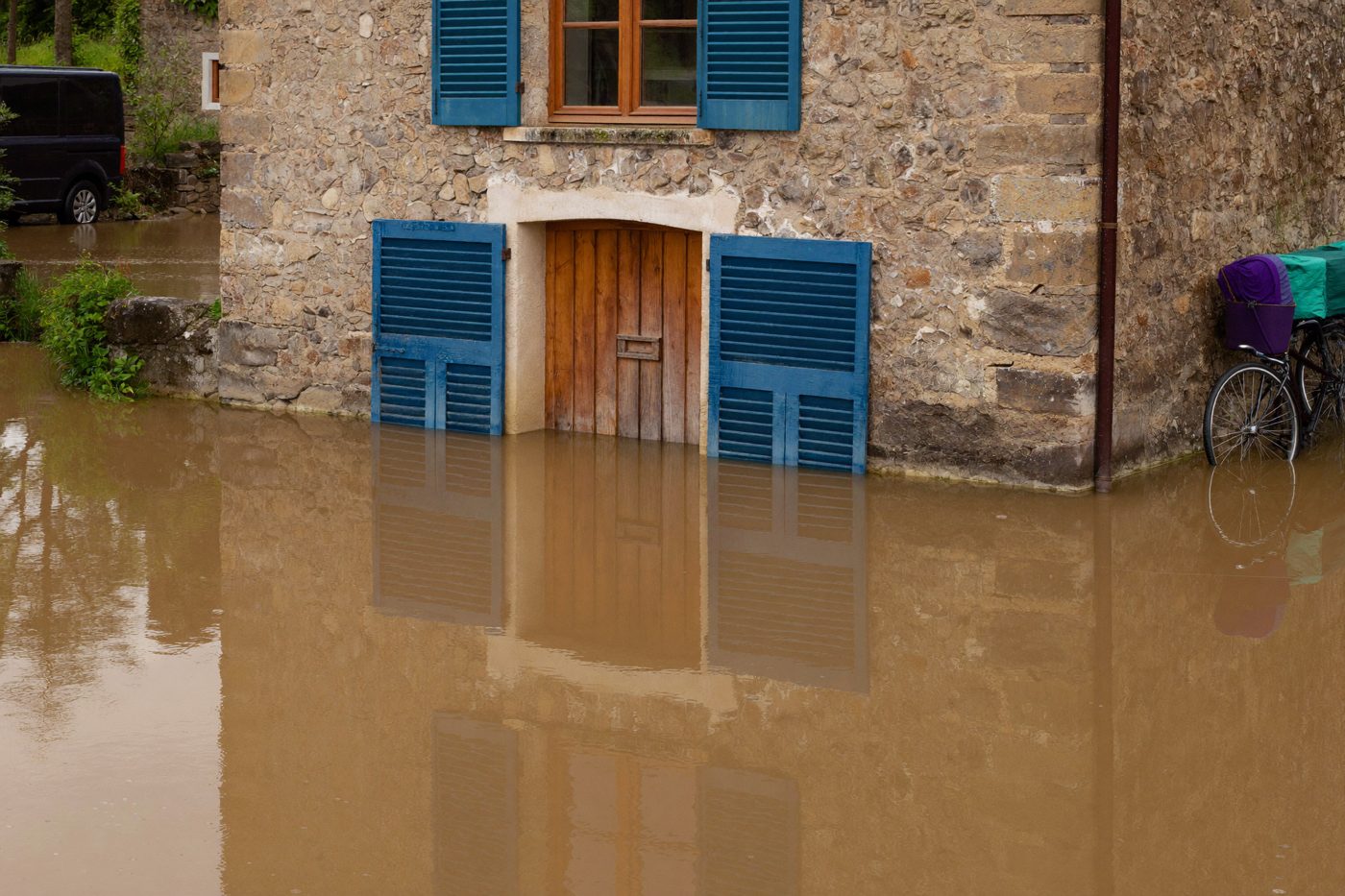 Façade en pierre aux volets bleus, l’eau boueuse montée jusqu’au bas de la porte d’entrée