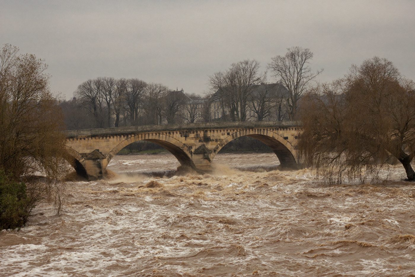 Rivière en crue, eau brune et rapide sous un pont de pierre — illustration générée
